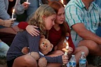 Mourners gather outside Annunciation Catholic School in Minneapolis, holding candles and flowers in memory of the victims of the Minnesota school shooting, as police secure the area and community members grieve together.