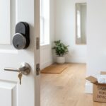 Retrofit smart lock on an apartment door and a smart plug powering a lamp, with a moving box nearby